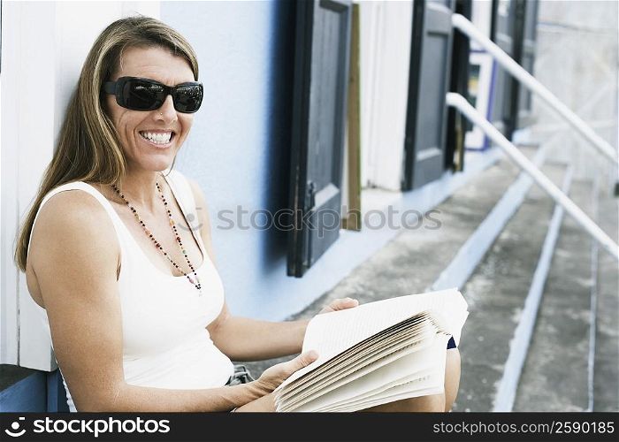 Mid adult woman sitting on steps and holding a book