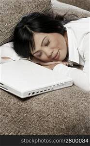 Mid adult woman sleeping on a couch with a laptop in front of her