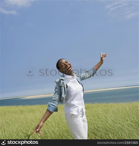 Mid adult woman standing on the beach with her arms outstretched and laughing