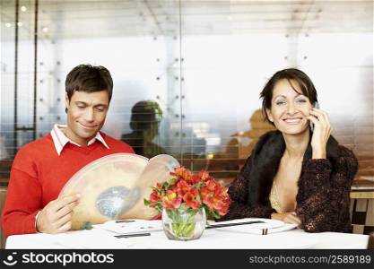 Mid adult woman talking on a mobile phone with a mid adult man looking at menu in a restaurant