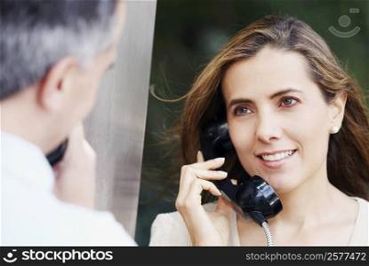 Mid adult woman talking on a pay phone with a mid adult man in front of her