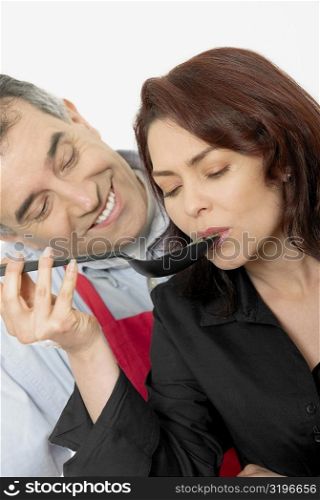 Mid adult woman tasting food with a spoon with a mid adult man looking at her