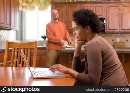 Mid adult woman using laptop while mid adult man cutting fruits