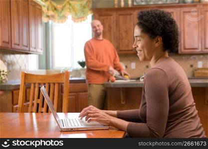 Mid adult woman using laptop while mid adult man cutting fruits
