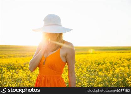 Mid adult woman using mobile phone in canola field wearing sunhat looking down