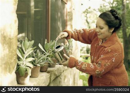 Mid adult woman watering plants with a watering can and smiling