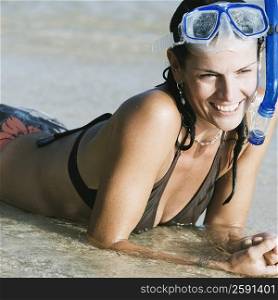 Mid adult woman wearing snorkeling gear and lying on the beach