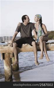 Mid adult woman with her arm around a mid adult man sitting on a jetty
