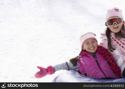 Mid adult woman with her daughter sliding down snowy slope on an inner tube