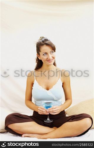 Mid adult woman witting on the bed and holding a glass of martini
