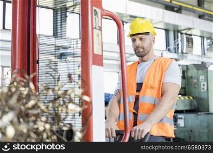 Mid adult worker pulling hand truck with steel shavings in factory