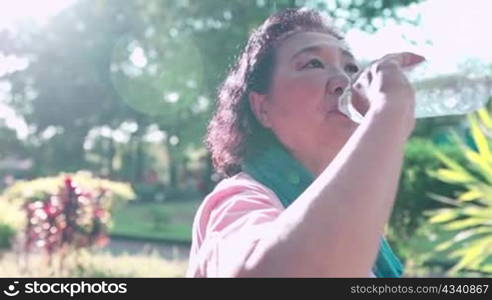 mid age asian woman drink fresh water from plastic bottle after doing exercise at the natural park garden, refreshing drink, retirement lifestyle rehydration, h2o mineral water, stay hydrated old age
