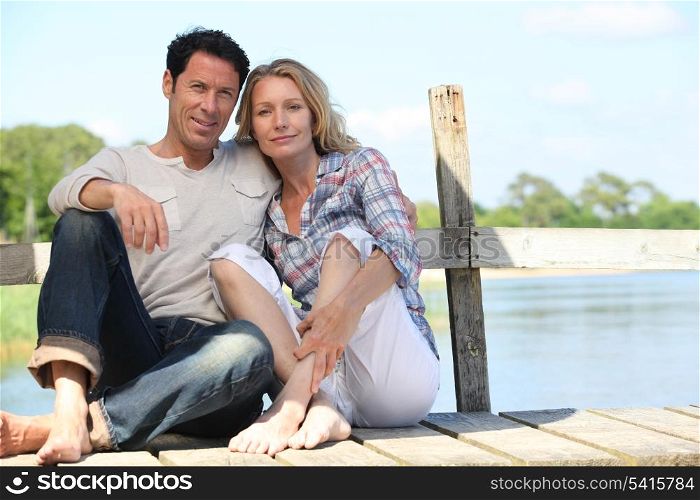 mid age couple seated on a pontoon near a lake