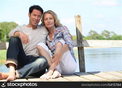 mid age couple seated on a pontoon near a lake