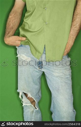 Mid body portrait of Caucasian man in torn blue jeans with hands in pockets.