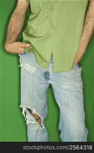 Mid body portrait of Caucasian man in torn blue jeans with hands in pockets.