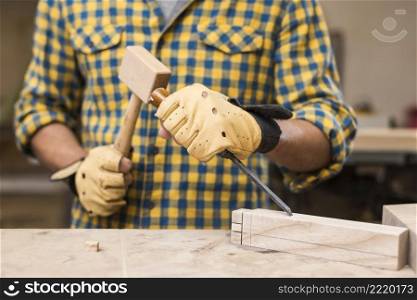 mid section male carpenter hitting chisel with hammer rectangular block