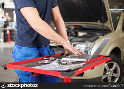 Mid section of mechanic working on laptop in a garage