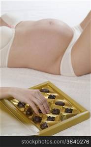 Mid section of pregnant woman on bed with chocolates