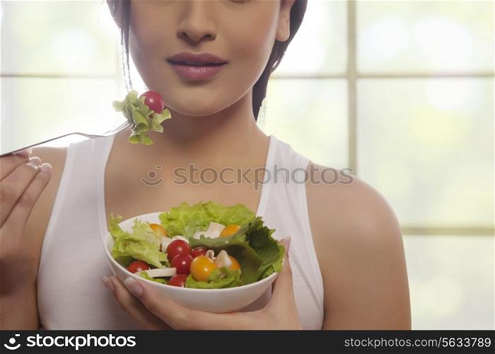Mid section of woman eating salad of lettuce, cherry tomatoes and mushrooms