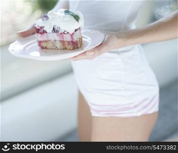 Mid section of woman with tasty raspberry cake in house