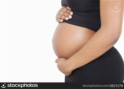 Mid section of young pregnant woman with hands on stomach over white background