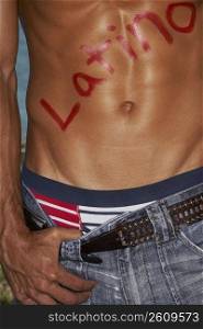 Mid section view of a bare chested young man with Latino written on his chest