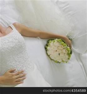 Mid section view of a bride lying on the bed and holding a bouquet of flowers