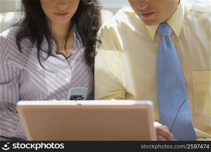 Mid section view of a businessman and a businesswoman sitting in front of a laptop
