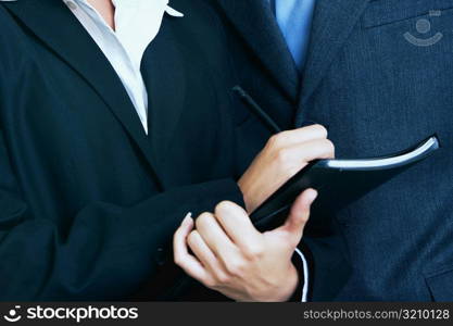 Mid section view of a businessman and a businesswoman standing together with a personal organizer