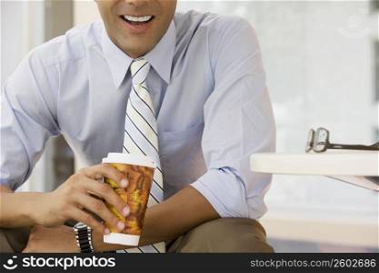 Mid section view of a businessman holding a coffee cup and smiling