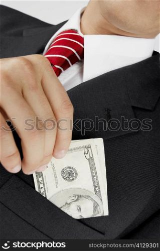 Mid section view of a businessman putting dollar bills in his pocket
