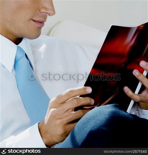 Mid section view of a businessman reading a magazine