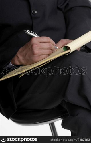 Mid section view of a businessman sitting on a stool and writing on a notepad