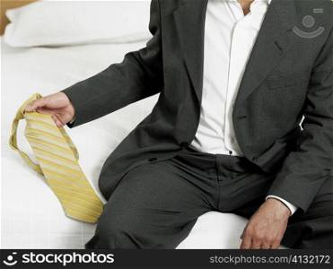 Mid section view of a businessman sitting on the edge of the bed and holding a tie