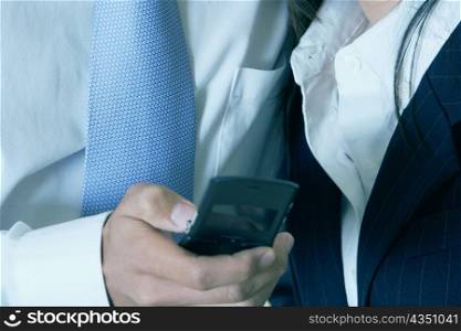 Mid section view of a businessman standing with a businesswoman and operating a mobile phone