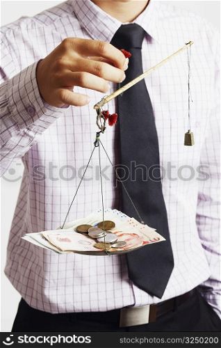 Mid section view of a businessman weighing paper currency with coins on a weighing scale