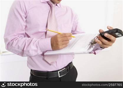 Mid section view of a businessman writing on a document and holding a mobile phone