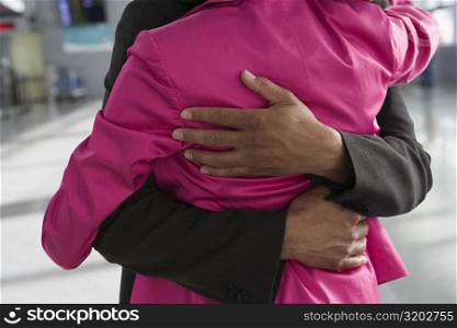 Mid section view of a businesswoman and a businessman embracing each other at an airport