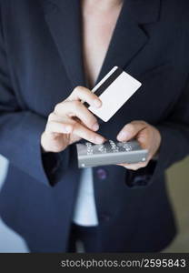 Mid section view of a businesswoman operating a calculator