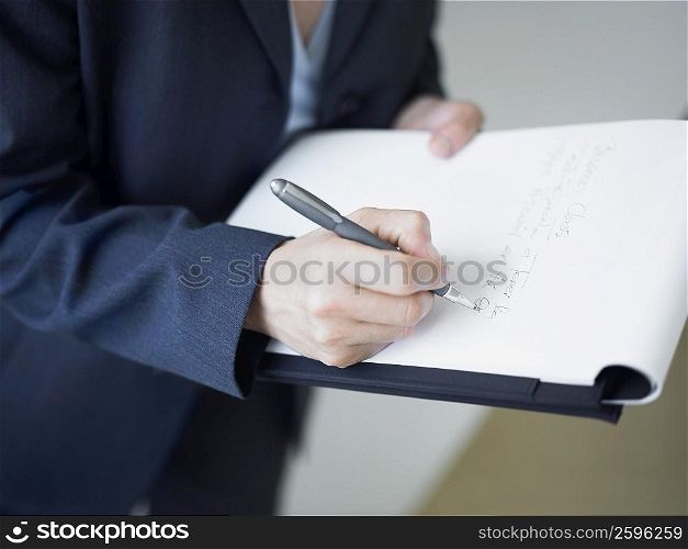 Mid section view of a businesswoman writing on a notepad