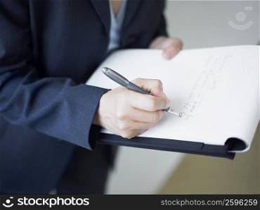 Mid section view of a businesswoman writing on a notepad