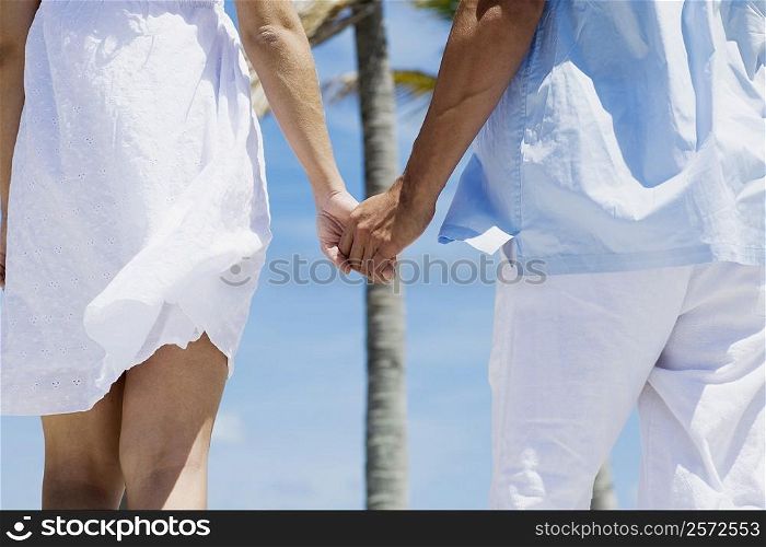 Mid section view of a couple holding hands of each other and walking on the beach