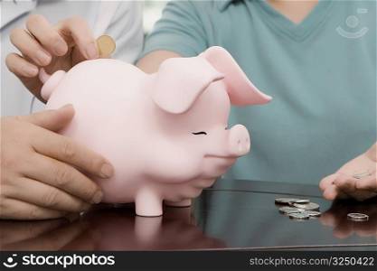 Mid section view of a couple putting a coin in a piggy bank