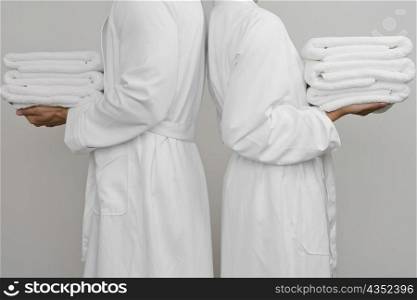 Mid section view of a couple standing back to back and holding folded towels