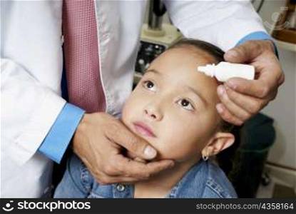 Mid section view of a doctor putting eye drops in a girl&acute;s eye