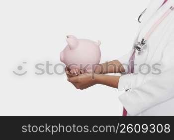 Mid section view of a female doctor holding a piggy bank