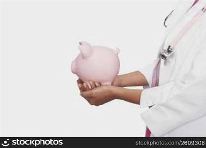 Mid section view of a female doctor holding a piggy bank