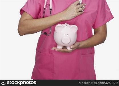Mid section view of a female nurse holding a piggy bank