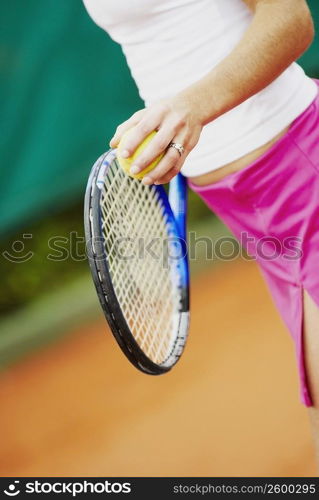 Mid section view of a female tennis player holding a tennis racket and a tennis ball